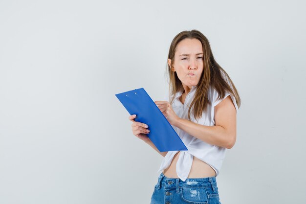 Young lady reading from paper while thinking in white blouse and looking confused. front view.