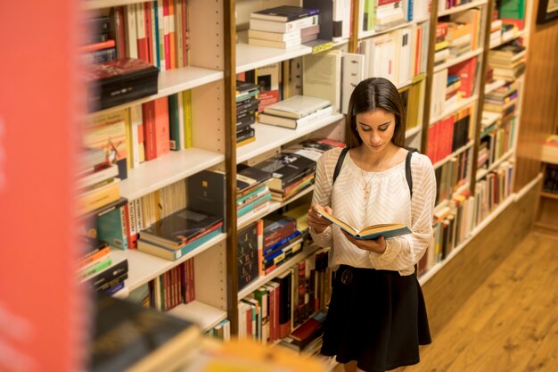 Young lady reading near bookshelf
