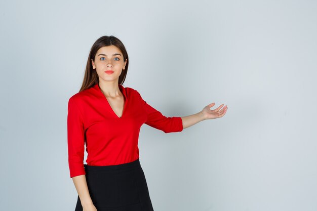 Young lady in red blouse, black skirt stretching hand as holding something