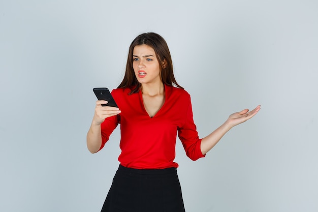 赤いブラウスの若い女性、携帯電話を見ているスカート