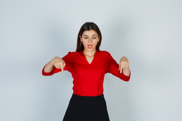 Young lady in red blouse, skirt pointing down and looking puzzled