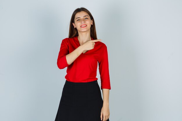 Young lady in red blouse, skirt pointing to the right side and looking joyful