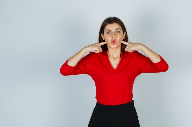 Young lady in red blouse, skirt pressing fingers on cheeks