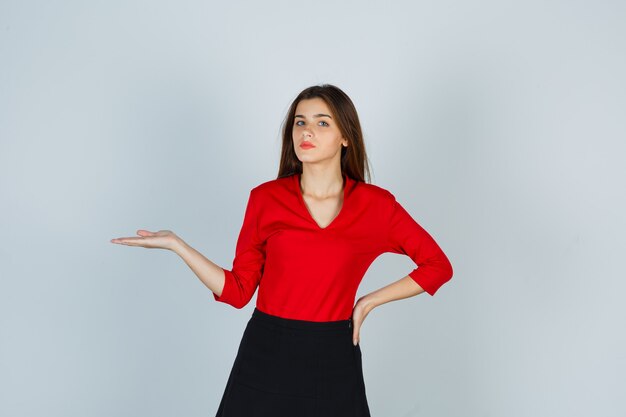 Young lady in red blouse, skirt pretending to hold something while keeping hand on hip