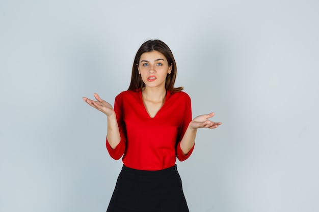 Free photo young lady in red blouse, skirt showing helpless gesture and looking hopeless