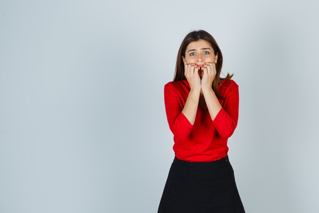 Free photo young lady in red blouse, skirt standing in scared pose and looking frightened
