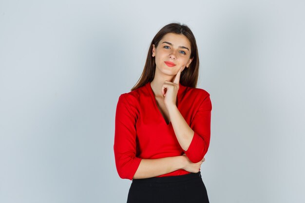 Young lady in red blouse, skirt standing in thinking pose and looking pensive