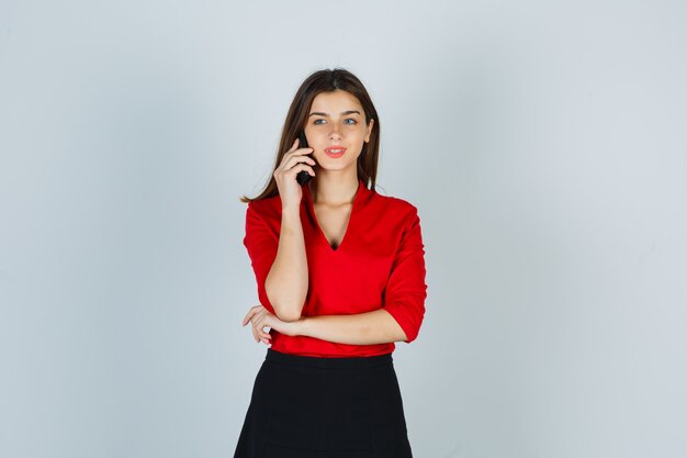 Foto gratuita giovane donna in camicetta rossa, gonna parlando al cellulare e guardando felice