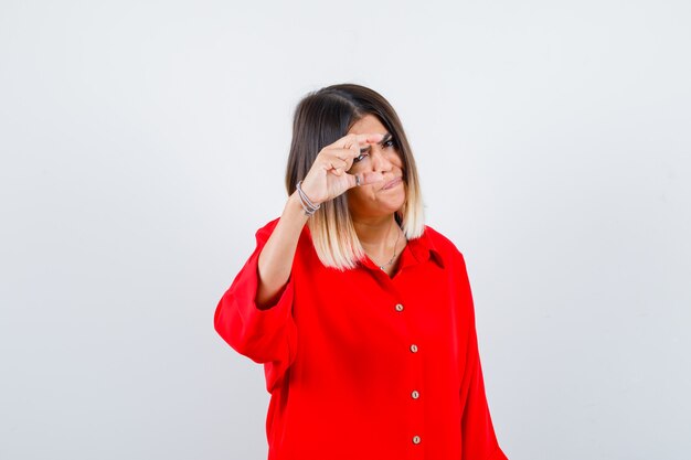 Young lady in red oversize shirt showing small size sign and looking serious , front view.