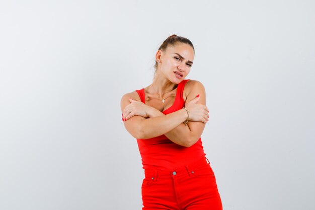 Young lady in red singlet, red trousers hugging herself and looking focused , front view.