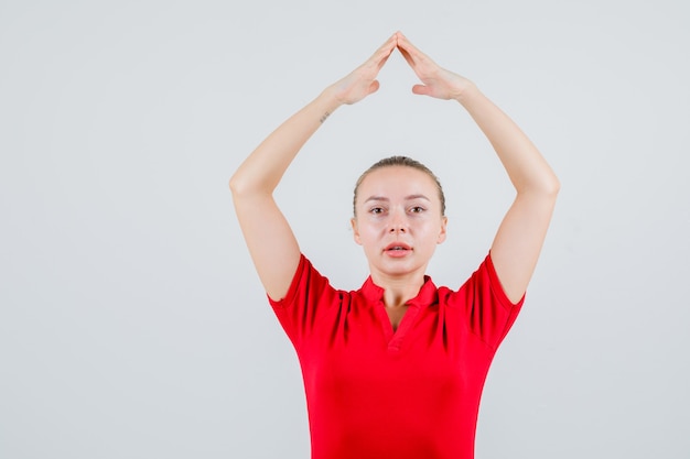 頭上で家の屋根のジェスチャーを作る赤いTシャツの若い女性