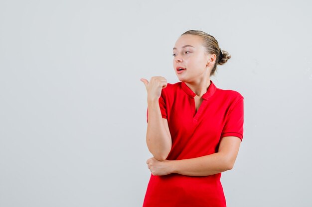 Young lady in red t-shirt pointing away and looking curious