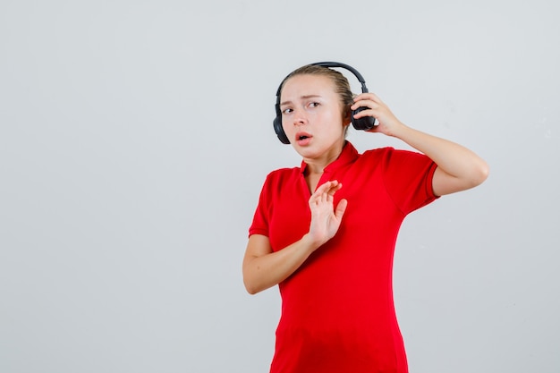 赤いTシャツを着た若い女性が停止ジェスチャーでヘッドフォンを脱いで怖がっています