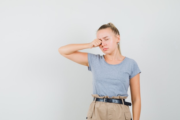 Tシャツとズボンで目をこすり、眠そうな若い女性