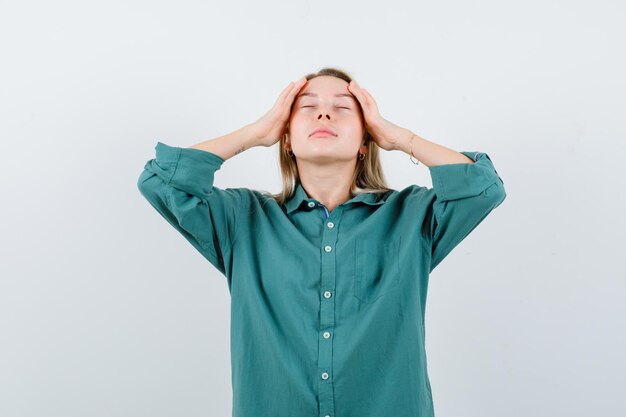 Young lady rubbing her temples in green shirt and looking relaxed