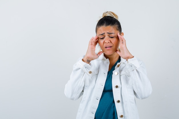 Young lady rubbing her temples in shirt, white jacket and looking painful , front view.