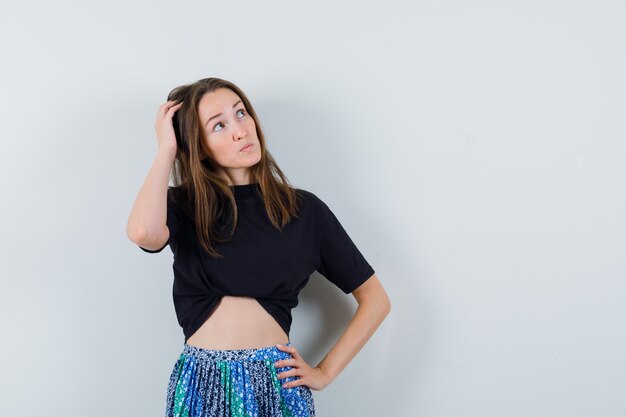 Young lady scratching head in blouse, skirt and looking indecisive