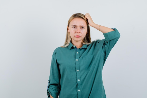 Young lady scratching head in green shirt and looking pensive