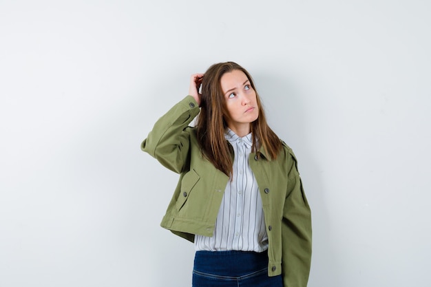 Young lady scratching head in shirt, jacket and looking indecisive, front view.