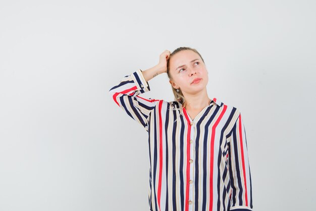 Young lady scratching head in striped shirt and looking pensive