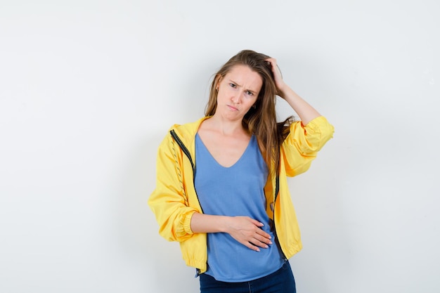 Young lady scratching head while scowling in t-shirt, jacket and looking hesitant