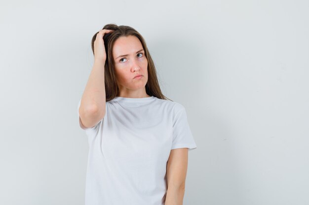 Young lady scratching head in white t-shirt and looking pensive  