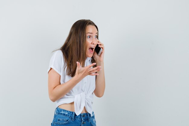 Young lady screaming while talking on phone in white blouse and looking nervous. front view.