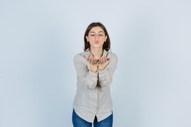 Young lady sending air kiss with cupped hands in casual, jeans and looking sincere. front view.