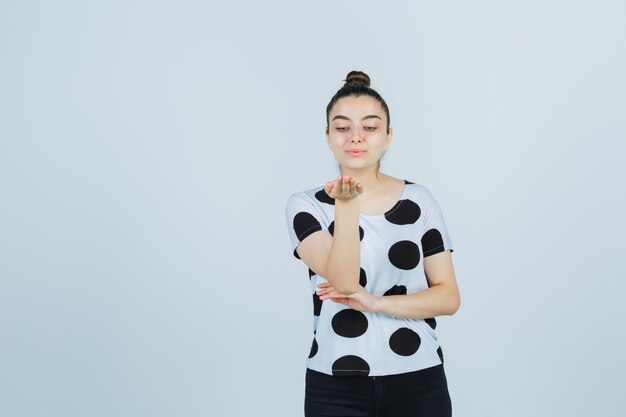 Young lady sending kiss with hand in t-shirt, jeans and looking pretty , front view.