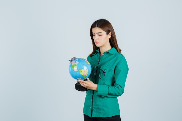 Молодая дама в рубашке держит земной шар и смотрит осторожно, вид спереди.