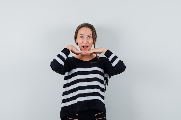 Young lady in shirt holding hands under chin and looking astonished