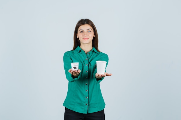 Молодая дама в рубашке держит пластиковые чашки кофе и выглядит довольным, вид спереди.