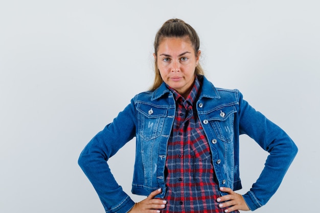 Young lady in shirt, jacket holding hands on waist and looking confident , front view.