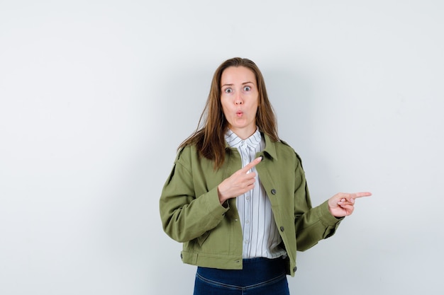 Foto gratuita giovane donna in camicia, giacca che punta da parte e sembra stupita, vista frontale.