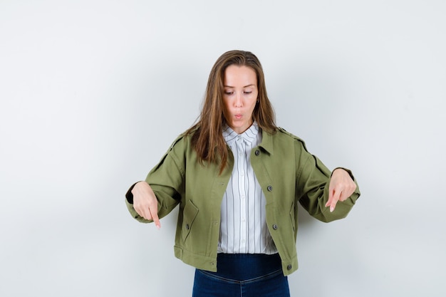 Young lady in shirt, jacket pointing down and looking focused , front view.