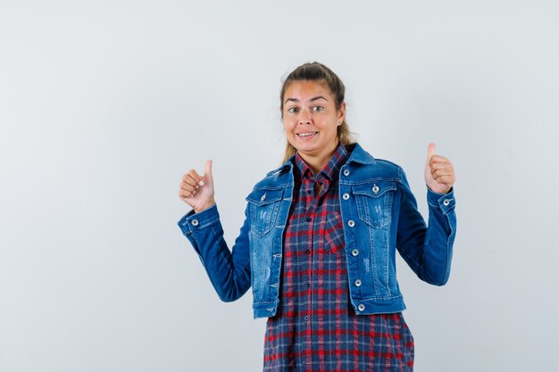 Young lady in shirt, jacket showing double thumbs up and looking merry , front view.