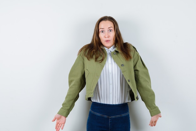 Giovane donna in camicia, giacca che mostra un gesto impotente scrollando le spalle e guardando confusa, vista frontale.