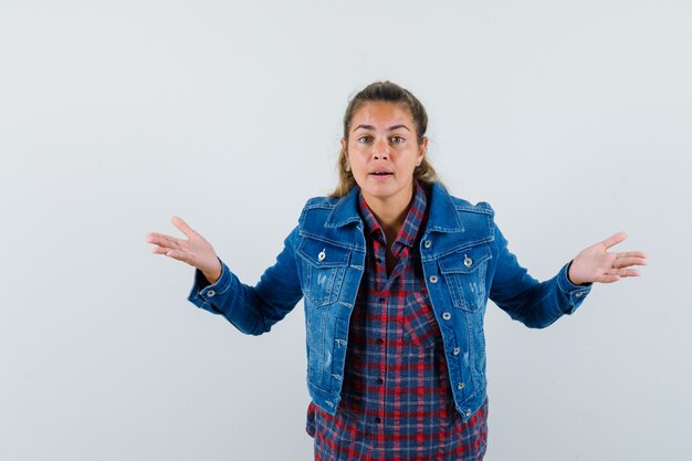 Young lady in shirt, jacket showing helpless gesture and looking confused , front view.