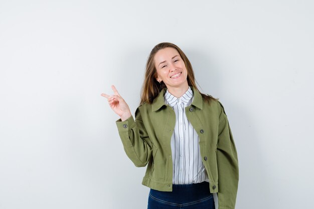 Young lady in shirt, jacket showing victory gesture and looking cheerful, front view.