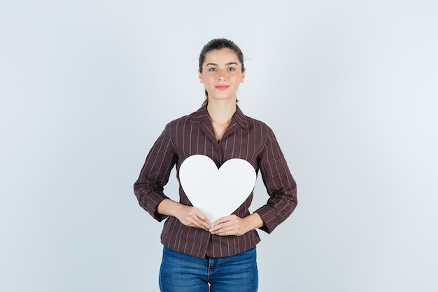 Young lady in shirt, jeans keeping paper poster and looking pleased , front view.