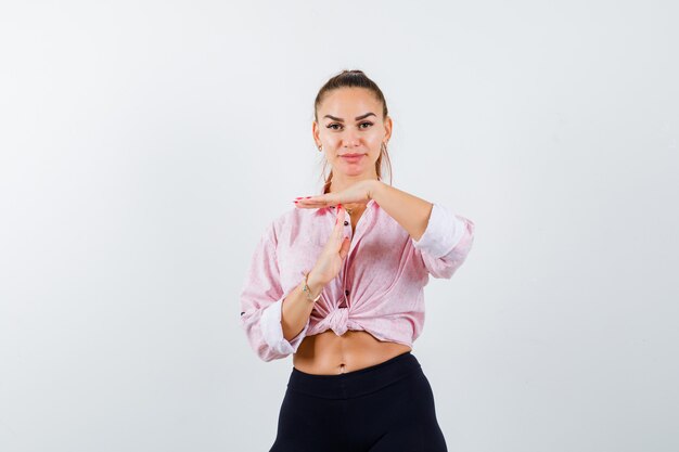 Young lady in shirt, pants showing time break gesture and looking confident , front view.