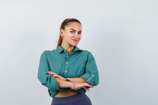 Young lady in shirt, pants with hands in front of herself and looking pleased , front view.