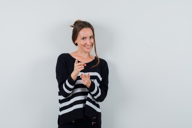 Young lady in shirt pointing at front and looking cheerful