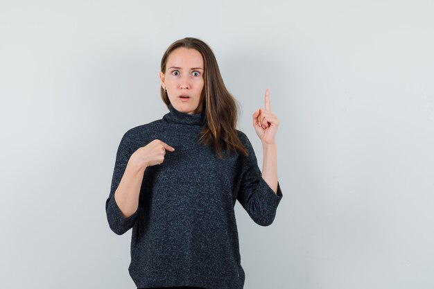 Young lady in shirt pointing at herself and up and looking puzzled