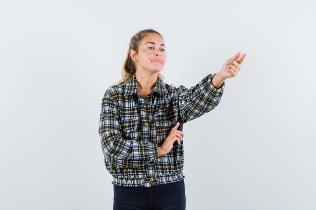 Young lady in shirt, shorts pointing away and looking confident , front view.