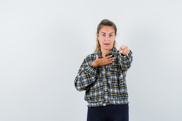 Young lady in shirt, shorts pointing at camera and looking confident , front view.