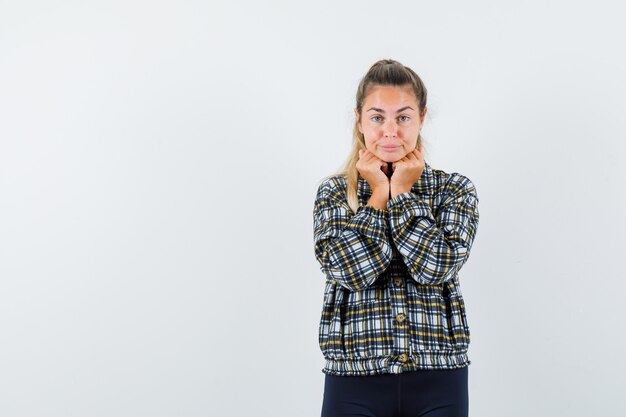 Young lady in shirt, shorts propping chin on fists and looking cute , front view.