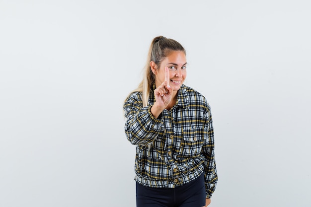 Foto gratuita giovane donna in camicia, pantaloncini che mostrano attesa su un gesto minuto con il dito in alto e guardando allegro, vista frontale.