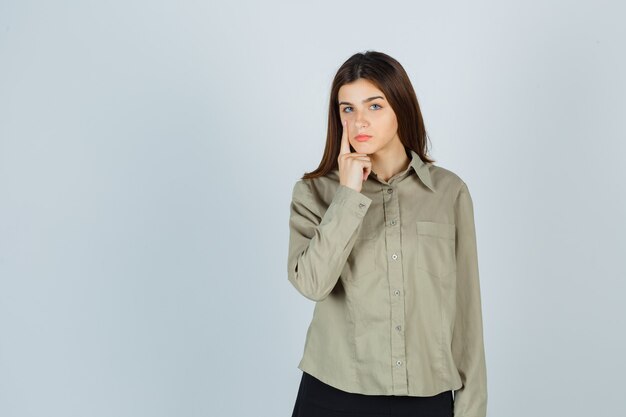 Young lady in shirt, skirt pointing at her eyelid and looking tired , front view.