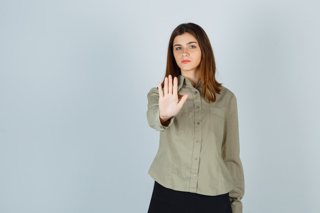 Young lady in shirt, skirt showing stop gesture and looking resolute , front view.